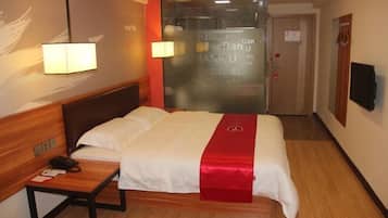 A hotel room with a bed, bedside table, lamp, and a glass door with a sign.