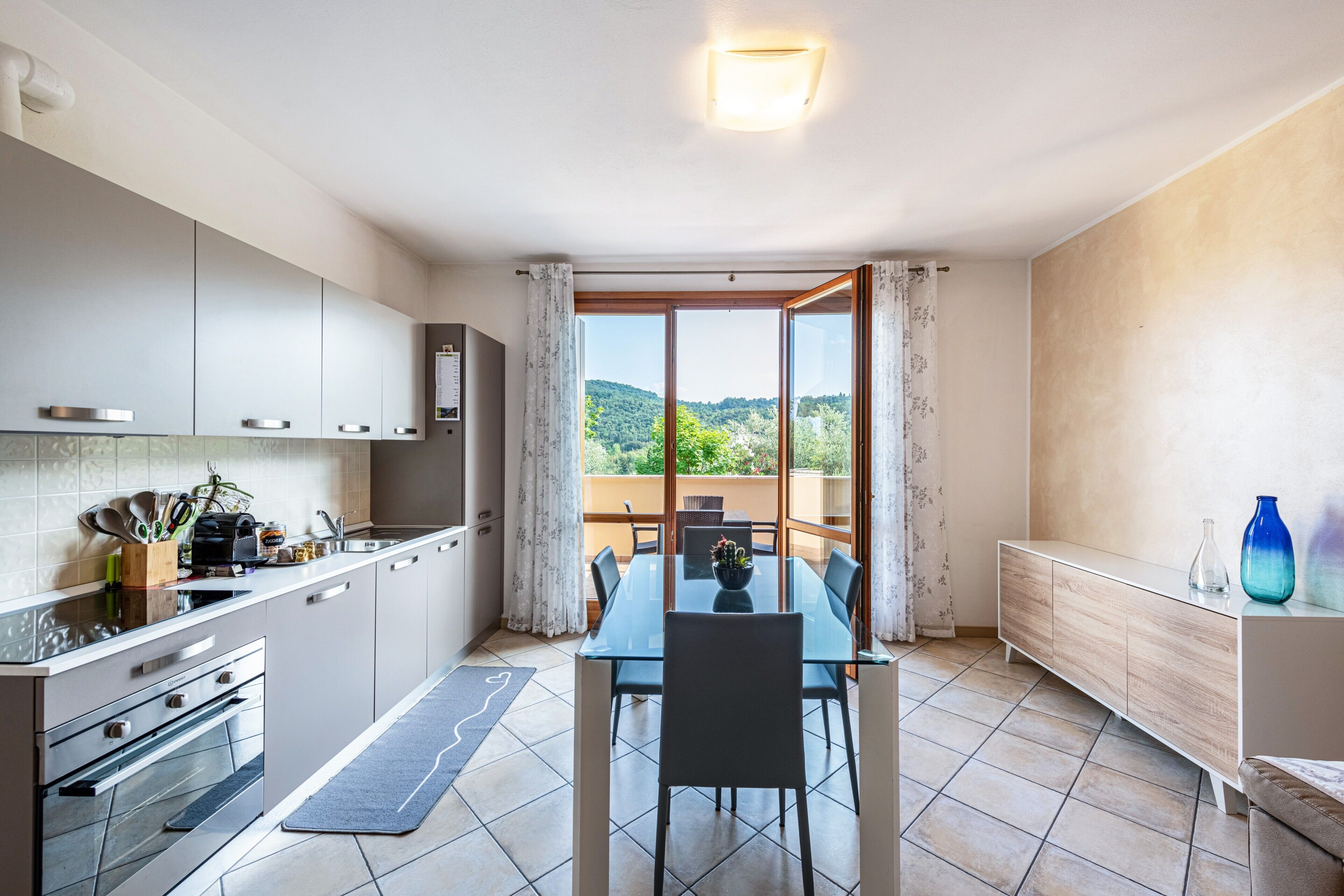 Eine moderne Küche mit Essbereich, Blick auf Grünflächen und einem Balkon mit Tisch und Stühlen.