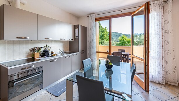 Une cuisine moderne avec une table à manger en verre, un four encastré et une vue sur un balcon aménagé en coin repas.