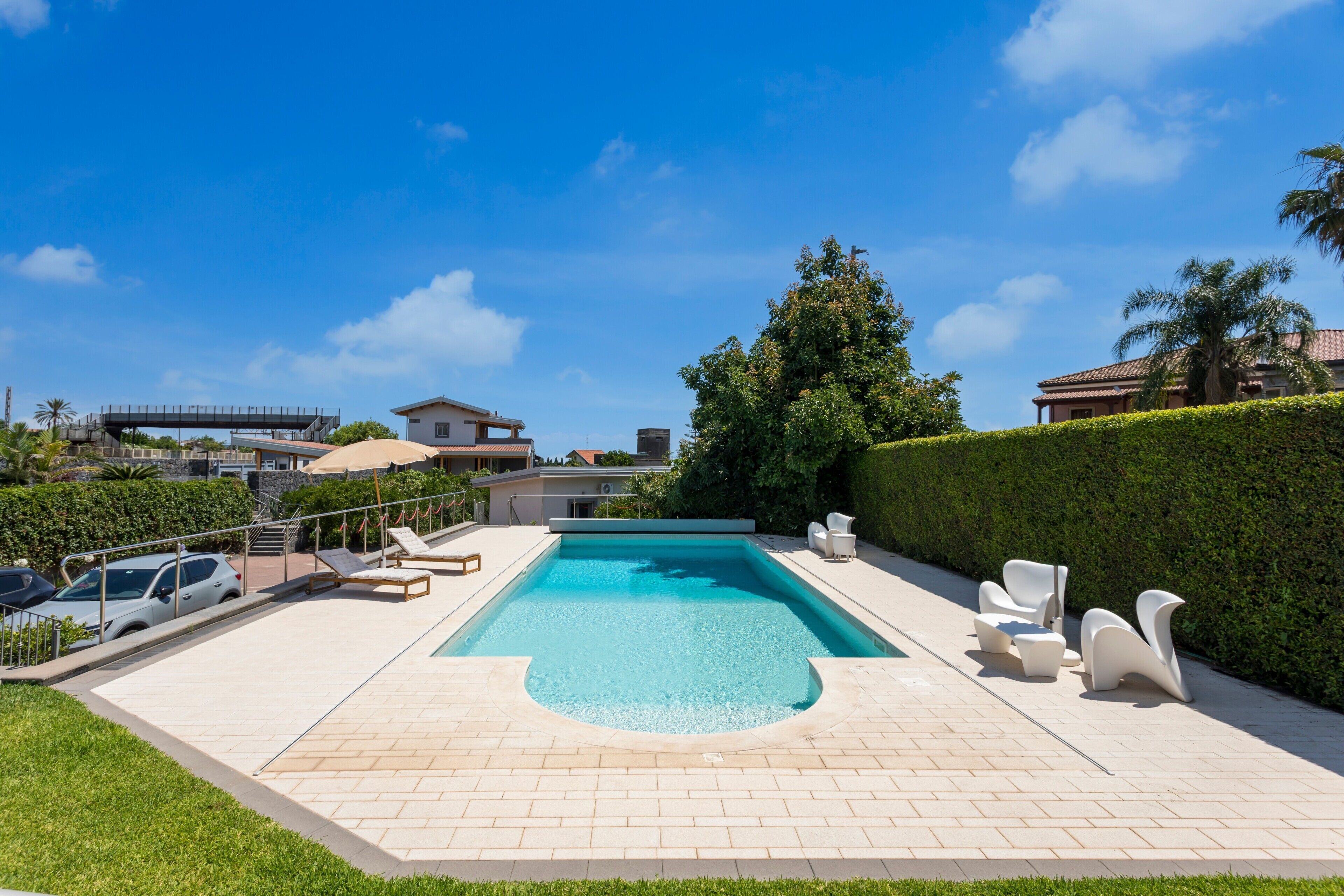 Una piscina con sillas de descanso, una terraza pavimentada y un cielo azul despejado.