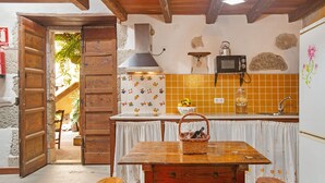 A rustic kitchen with a wooden table, a microwave, and a stone wall.