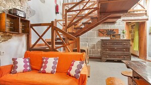 A cozy room with a wooden staircase, a sofa with patterned cushions, a wooden table, and a stone fireplace.
