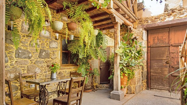 A stone building with a wooden table and chairs, surrounded by potted plants and a stone wall.