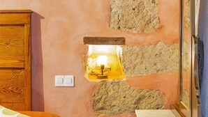 A room with a wooden cabinet, a stone wall with a light fixture, a white switch, and a mirror.