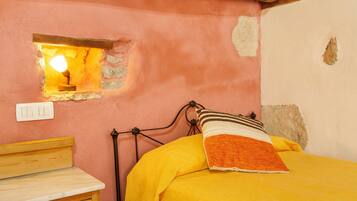 A bedroom with a bed, a nightstand, a wall-mounted lamp, and a small window.