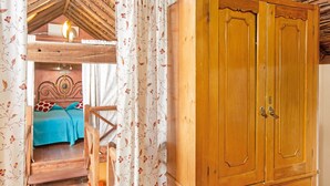 A bedroom with a wooden wardrobe, a bed with a blue bedspread, and a staircase leading to an upper room.
