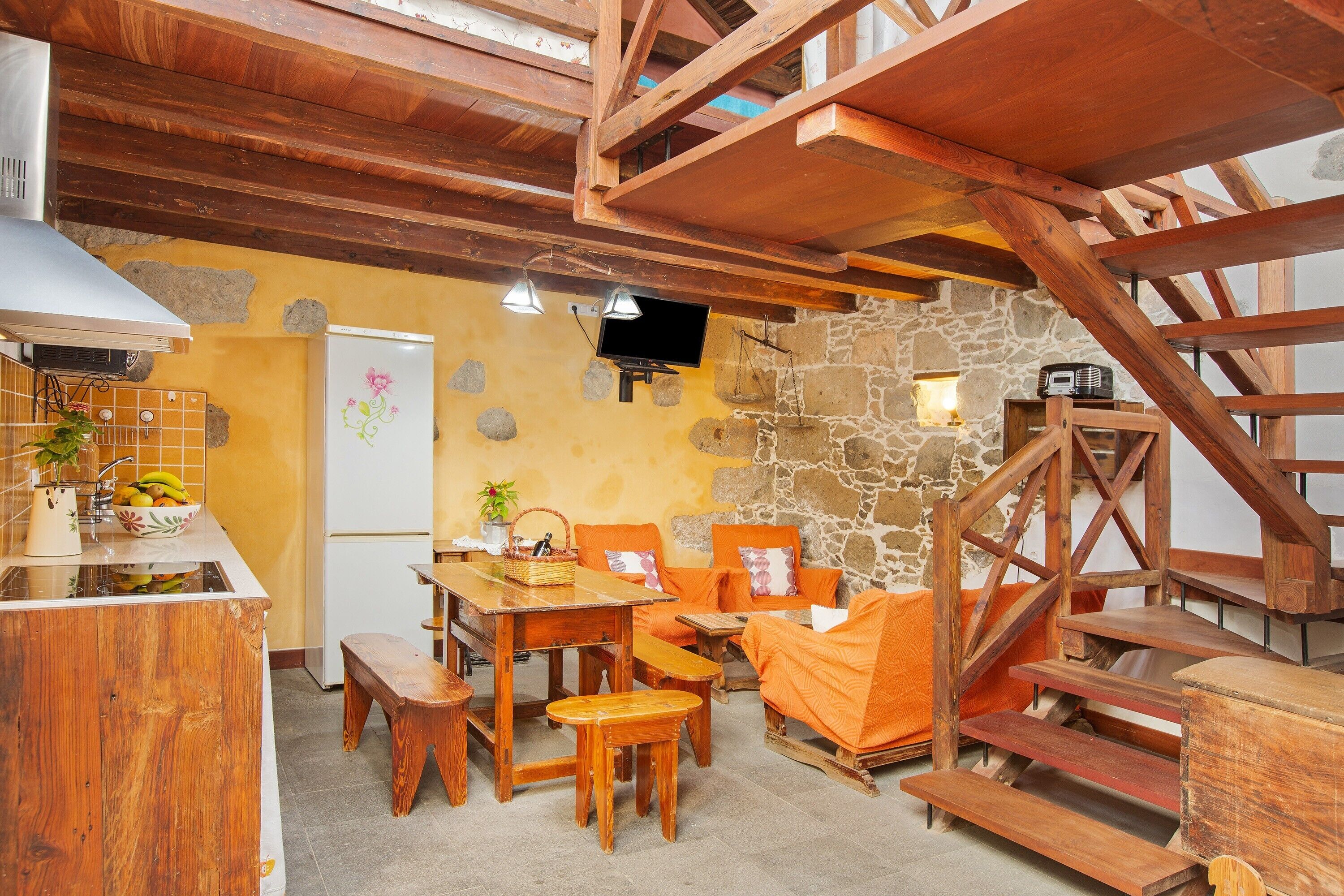 A rustic interior with wooden beams, a stone wall, a kitchen area, and a seating arrangement.