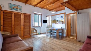A spacious living area with wooden flooring, a dining table, and a kitchen in the background.