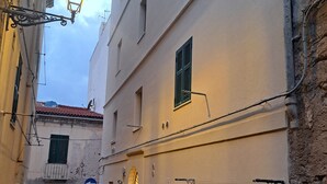 A narrow cobblestone street flanked by buildings with barred windows and a street lamp.