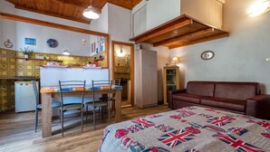 A cozy room with a wooden ceiling, a dining table with chairs, a bed with a quilt, and a red leather sofa.