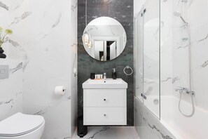 Une salle de bain avec des toilettes blanches, un lavabo avec un miroir au-dessus et un espace douche.