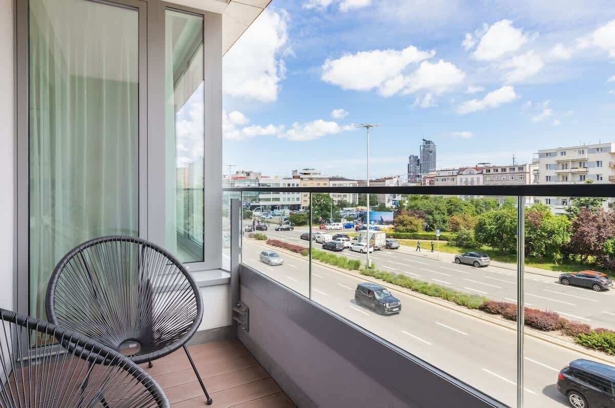 A balcony with a view of a city street, a chair, and a window with curtains.