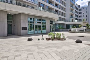 Un bâtiment moderne doté d’une façade incurvée, de grandes fenêtres en verre et d’une cour dallée agrémentée de bornes et de petites plantes.