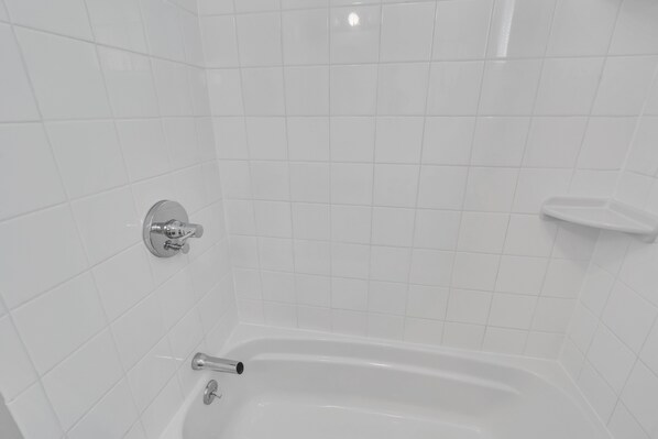 Un baño con paredes de azulejos blancos, una bañera y un grifo cromado.