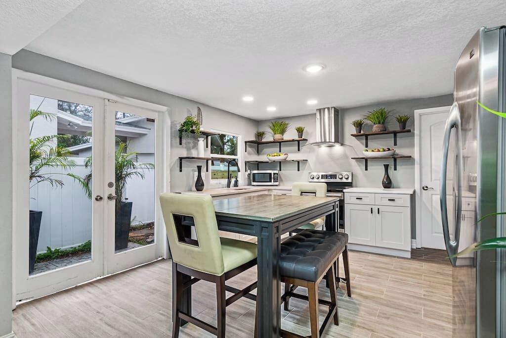 A modern kitchen with white cabinets, a stainless steel refrigerator, and a dining area with a table and chairs.