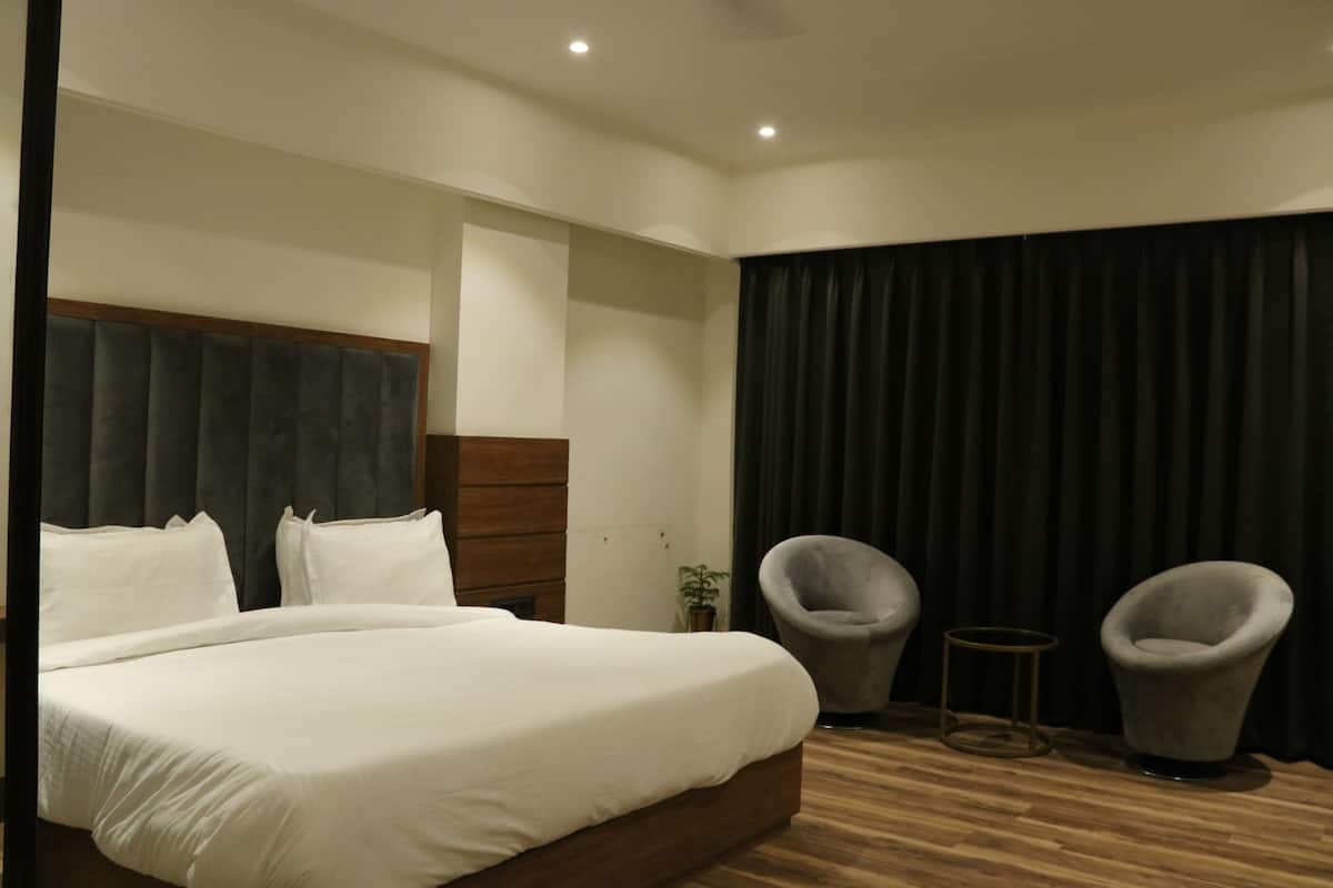 Ein Hotelzimmer mit einem großen Bett, zwei Sesseln, einem kleinen Tisch und einem dunklen Vorhang.