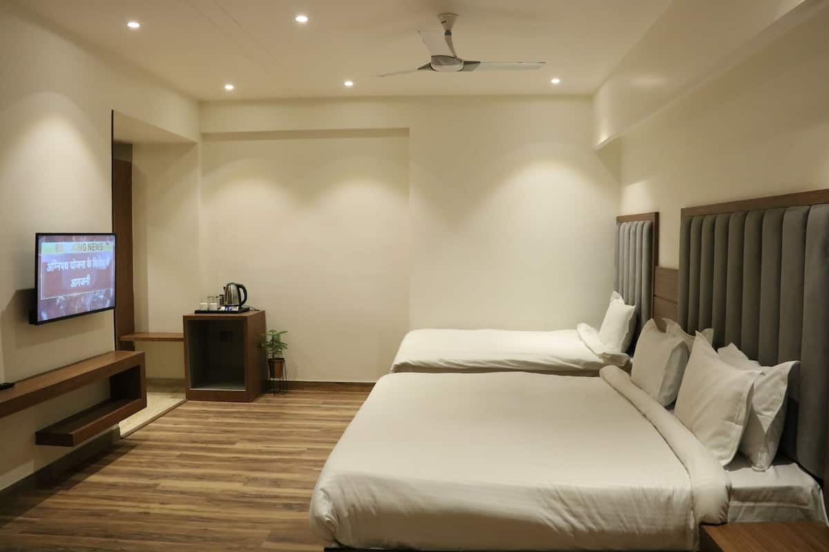 Ein Hotelzimmer mit zwei Betten, einem an der Wand befestigten Flachbildfernseher, einem Deckenventilator und einem kleinen Tisch mit einer Pflanze.