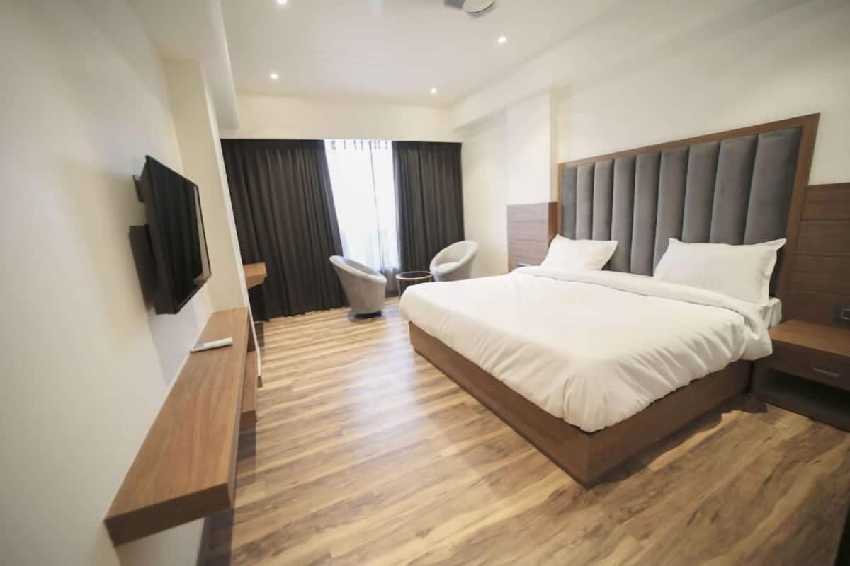 Ein modernes Hotelzimmer mit einem großen Bett, einem Flachbildfernseher an der Wand, einer hölzernen Bank und einem Sessel.