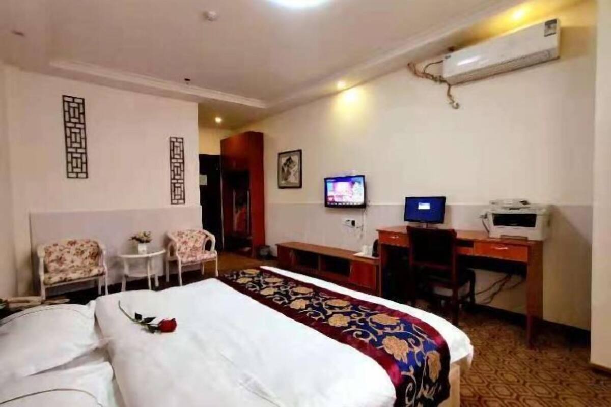 A hotel room with a bed, a desk, a chair, a television, and an air conditioning unit.