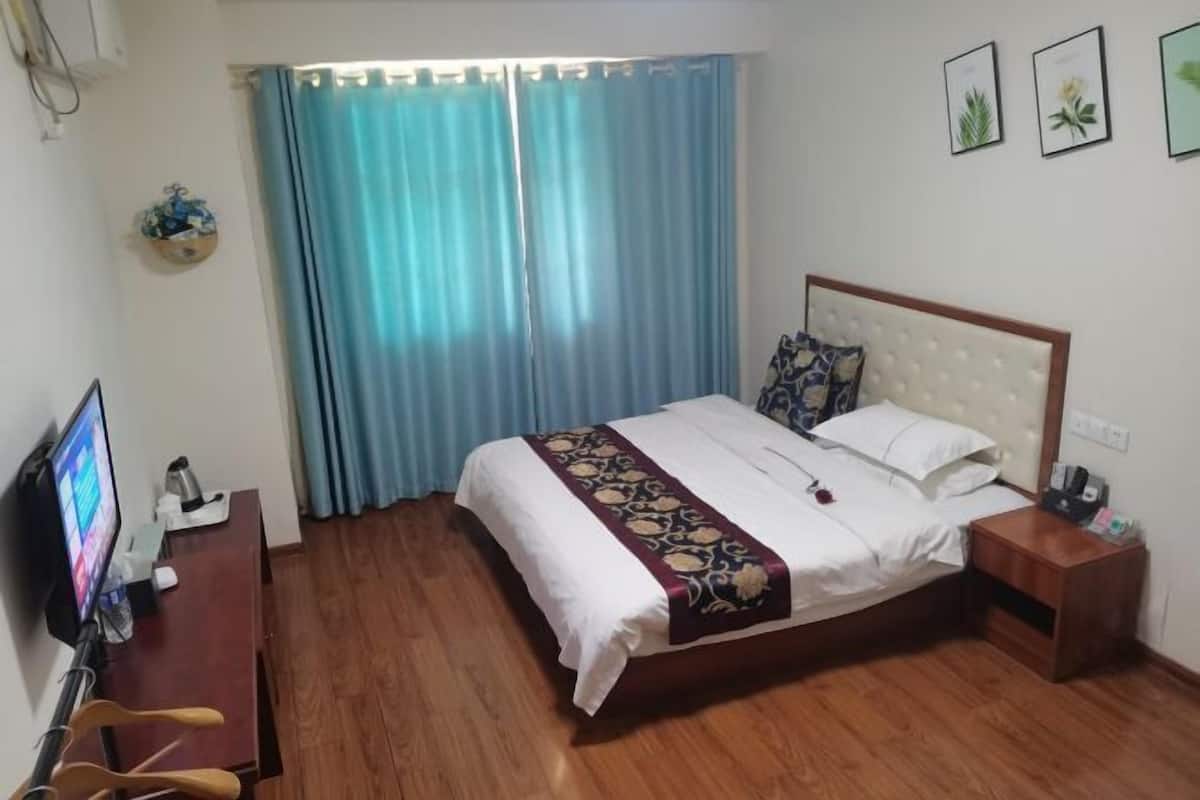 A hotel room with a bed, a desk with a computer, a TV, and a window with curtains.