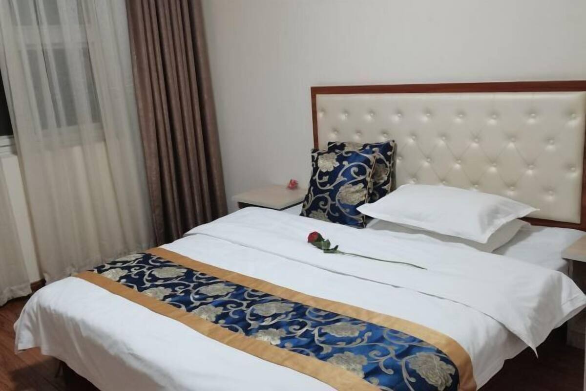 A hotel room with a large bed, a headboard, a bedside table, and a window with curtains.