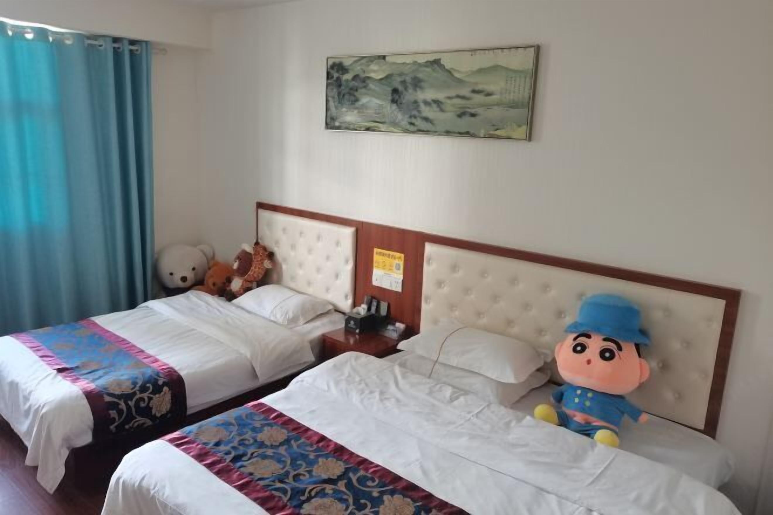 A hotel room with two beds, a large teddy bear on one bed, a plush toy on the other, and a painting on the wall.