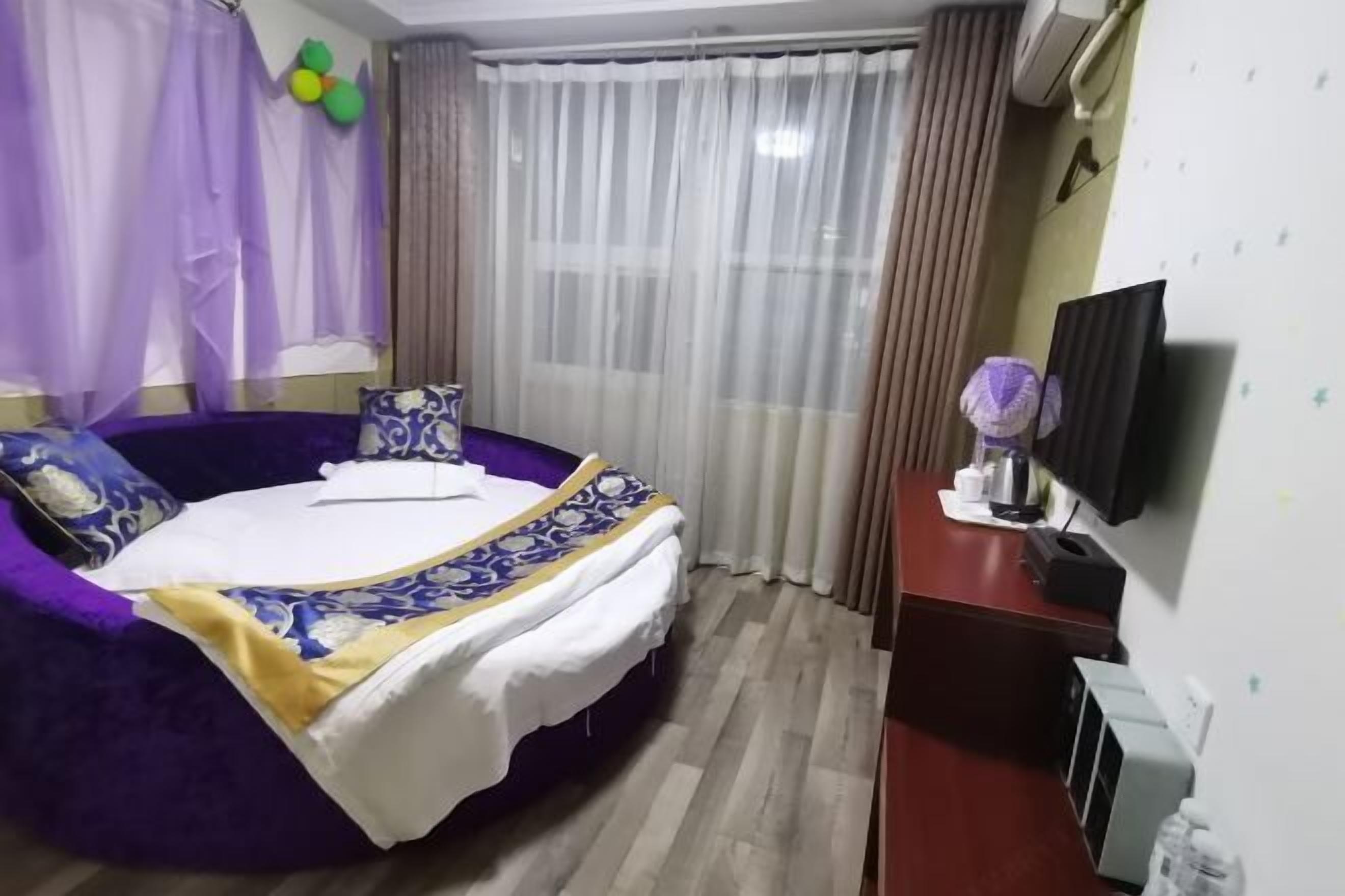 A bedroom with a large bed, a desk with a television, and a window with curtains.