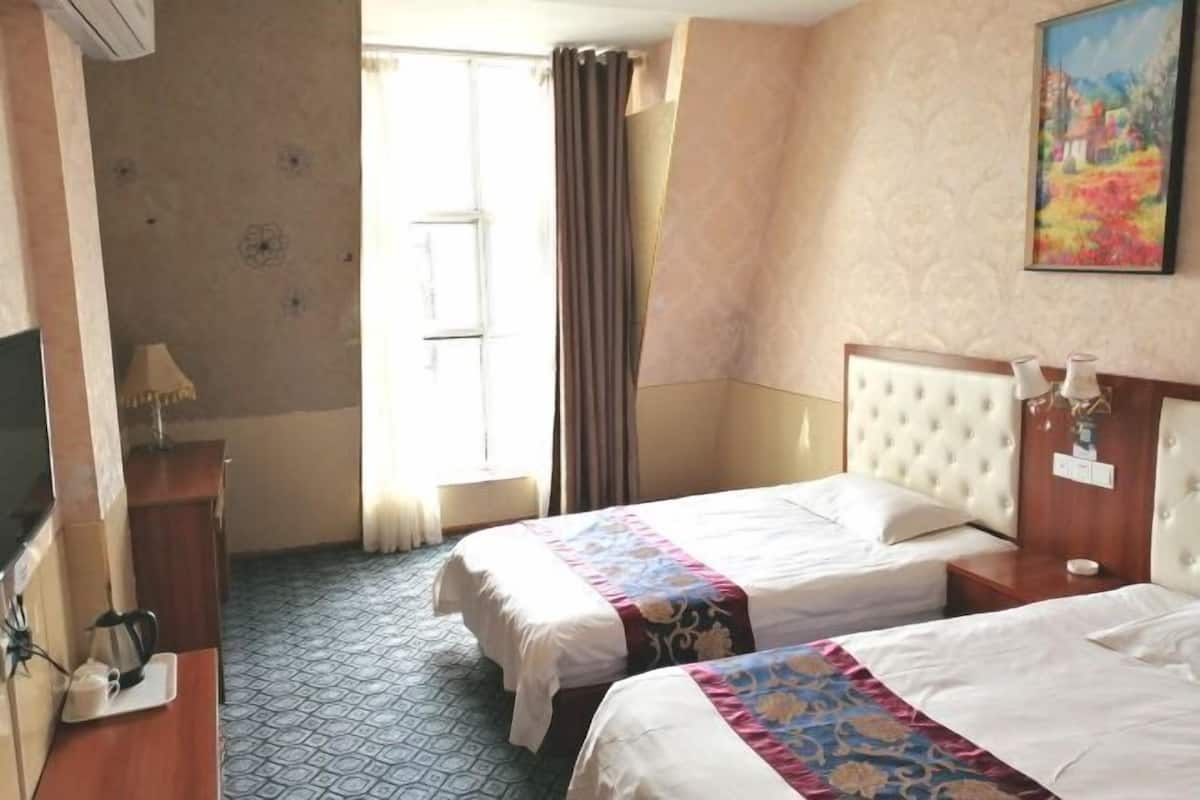A hotel room with two beds, a television, a desk, and a window with curtains.