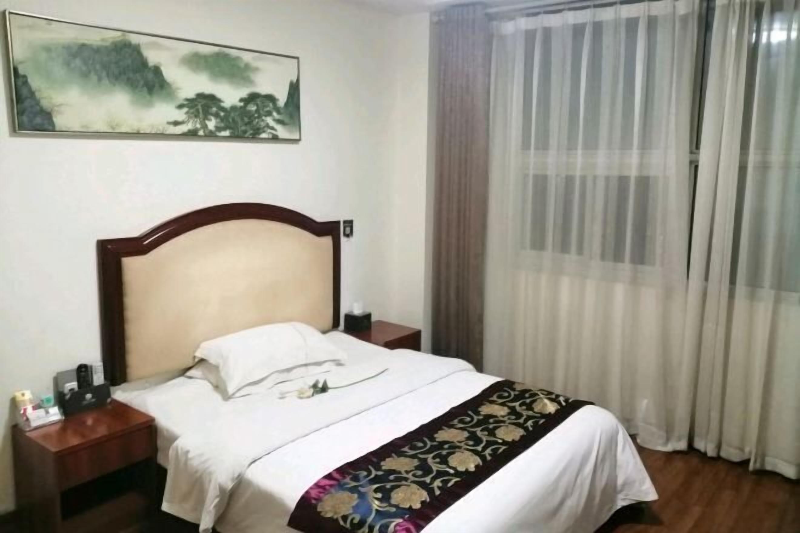 A hotel room with a bed, a nightstand, a painting on the wall, and a window with curtains.