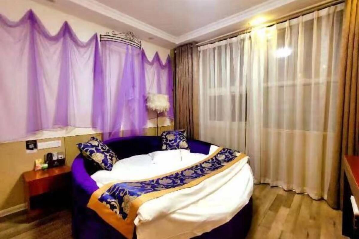 A hotel room with a bed, a nightstand, a lamp, and curtains.