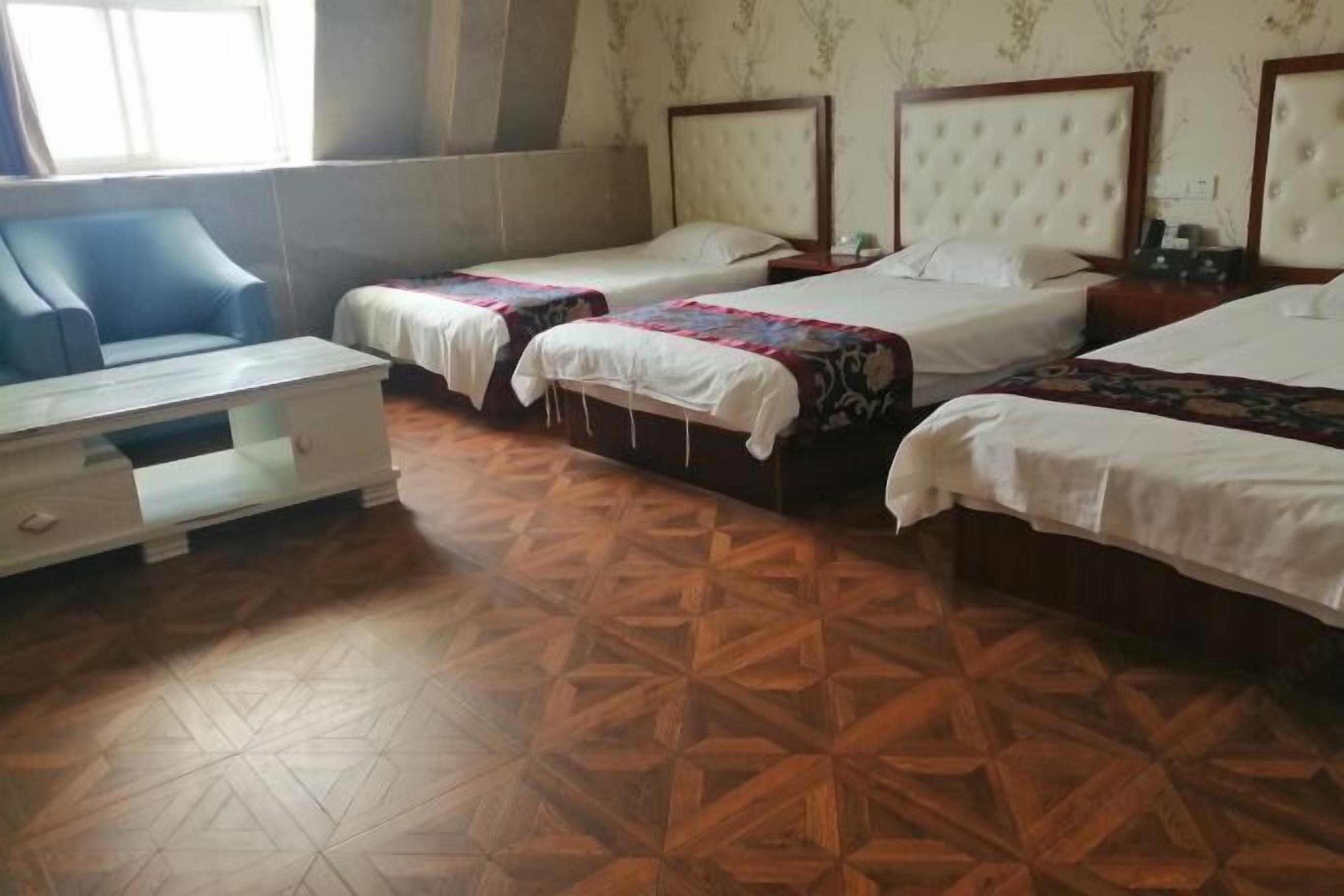 A hotel room with two single beds, a sofa, a wooden patterned floor, and a window with curtains.