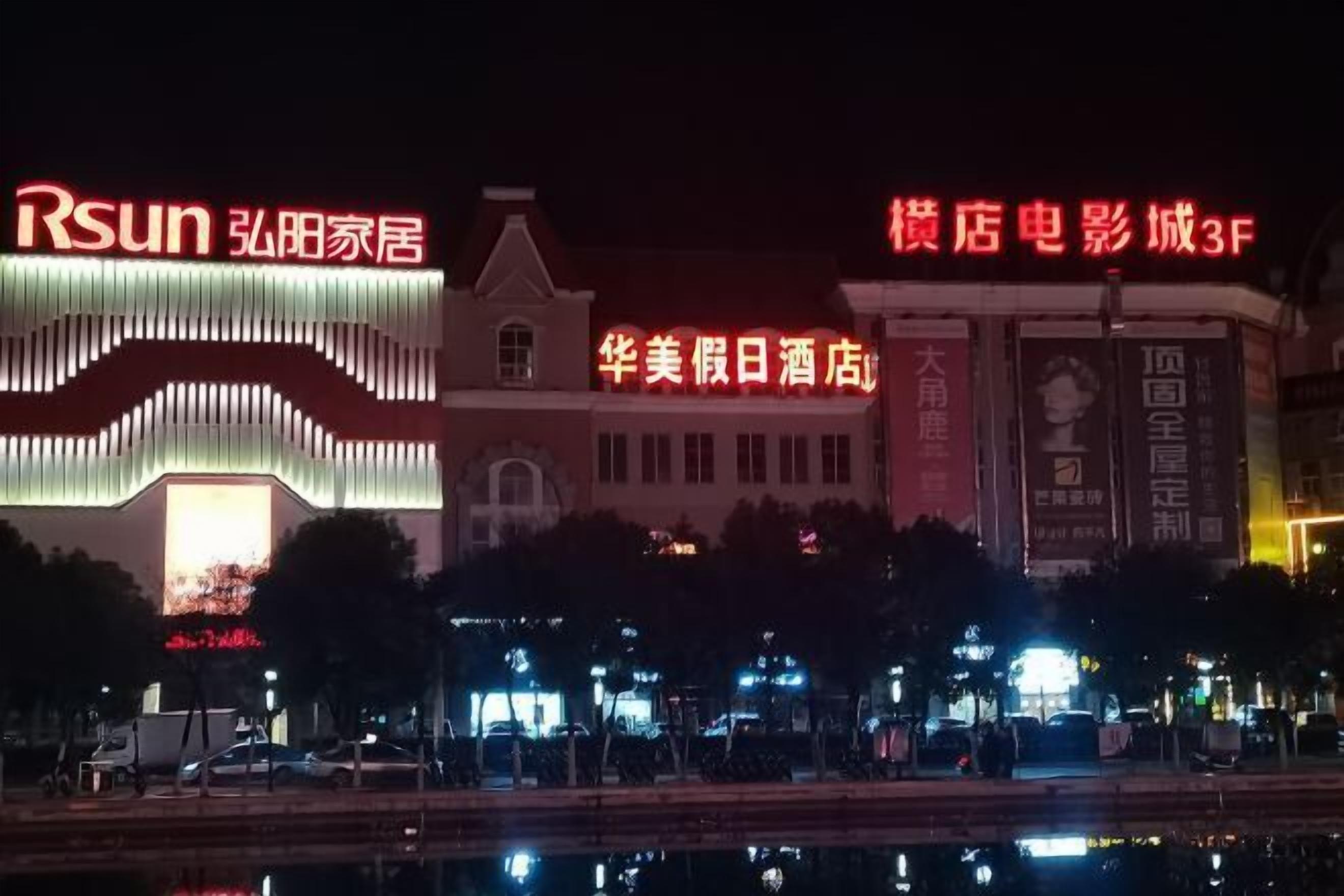 A hotel with illuminated signage, a large digital display, and a reflection in the water.