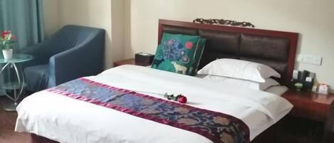 A neatly made bed with a floral bedspread, a blue armchair, and a small round table with a potted plant.