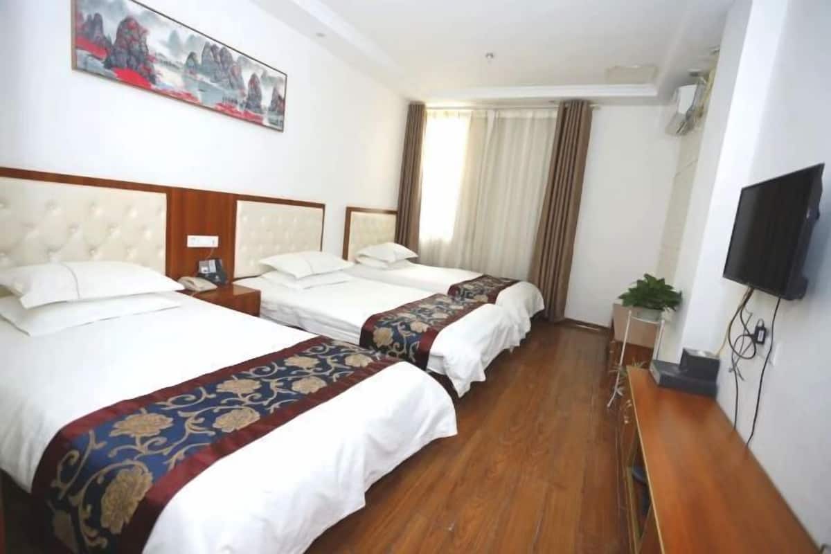 A hotel room with two beds, a flat-screen TV, a small table with a plant, and a painting on the wall.