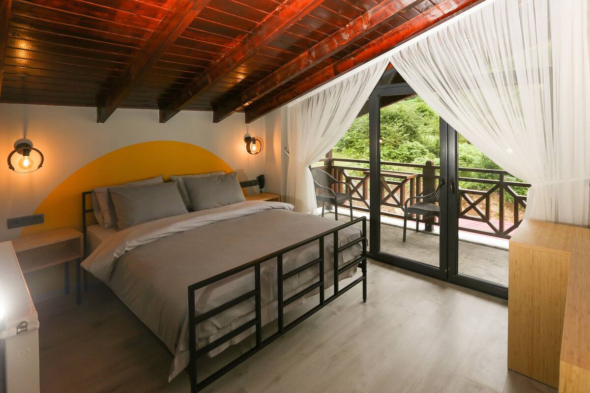 A bedroom with a bed, bedside lamps, a wooden ceiling, and a balcony with a table and chairs.