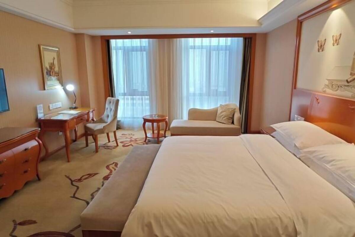 Habitación de hotel con una cama grande, un escritorio con silla, una mesita y un sofá.