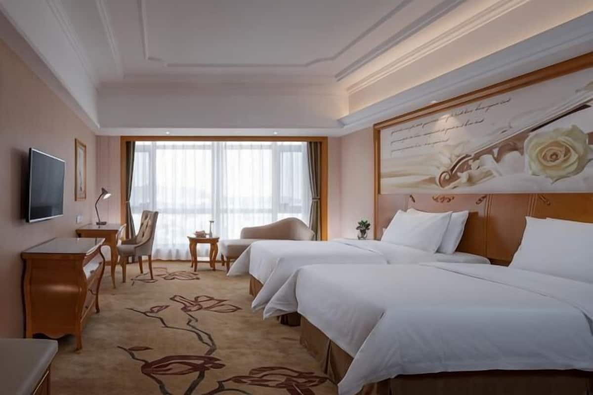 Habitación de hotel con dos camas, un escritorio, una silla, un televisor y un ventanal grande.