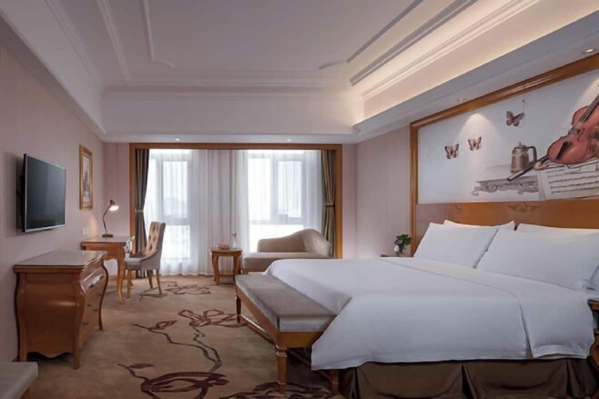 Habitación de hotel con una cama grande, un escritorio, una silla, un televisor y una ventana con cortinas.