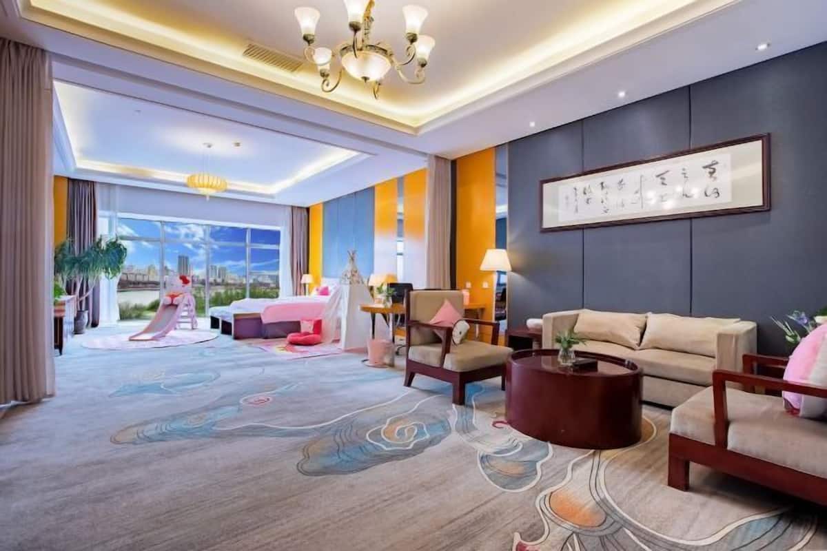Um hall de hotel com uma janela grande, um sofá, uma poltrona, uma mesa de centro e um tapete decorativo.