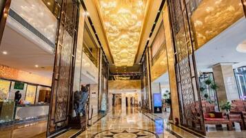 A hotel lobby with a marble floor, a reception desk, and a large chandelier.