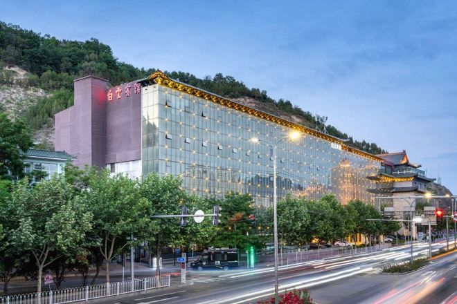 Un hotel moderno con facciata in vetro, situato vicino a un edificio tradizionale e una strada trafficata.