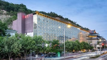 A modern hotel with a glass facade, located near a traditional building and a busy street.