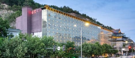 Un hotel moderno con fachada de vidrio, situado cerca de un edificio tradicional y una calle concurrida.