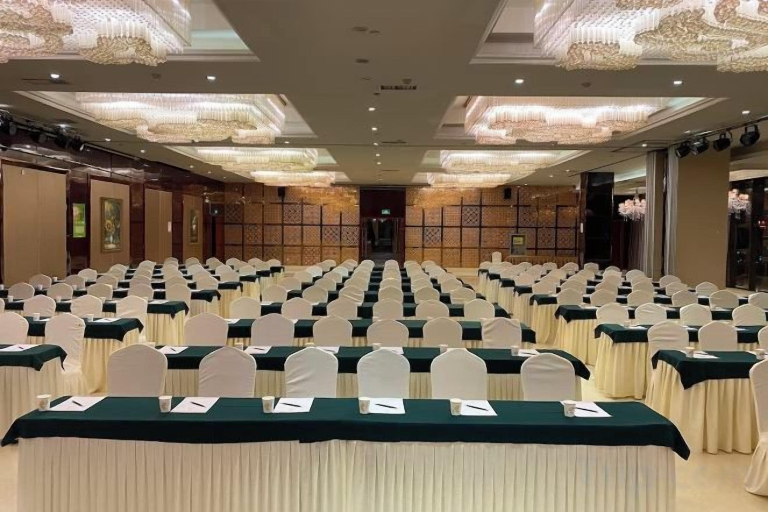 A conference room with rows of tables and chairs, a chandelier, and a traditional Asian-style wall.