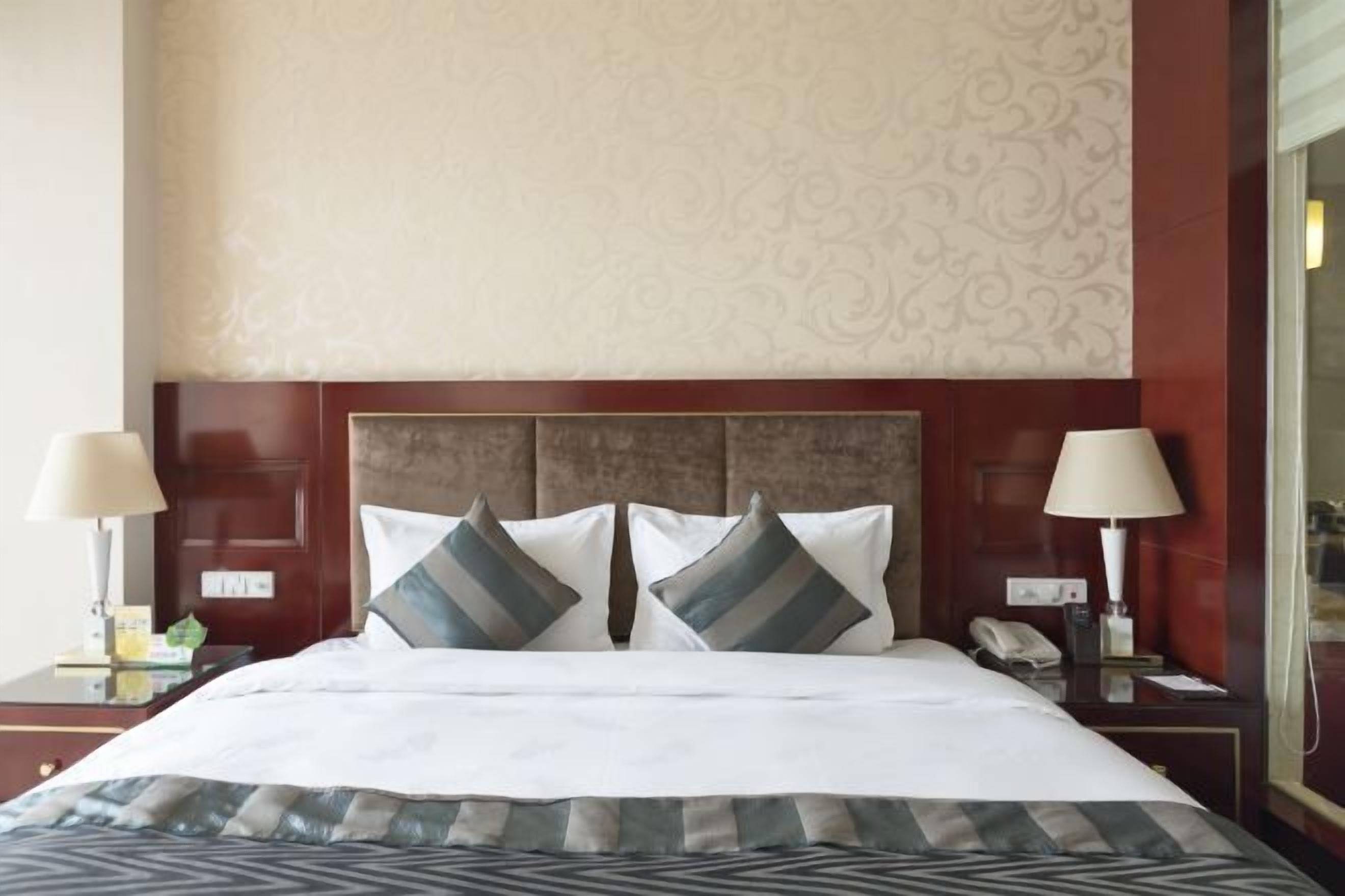 Ein Hotelzimmer mit einem großen Bett, zwei Nachttischen, einem Telefon und einer Wand mit einem dekorativen Muster.