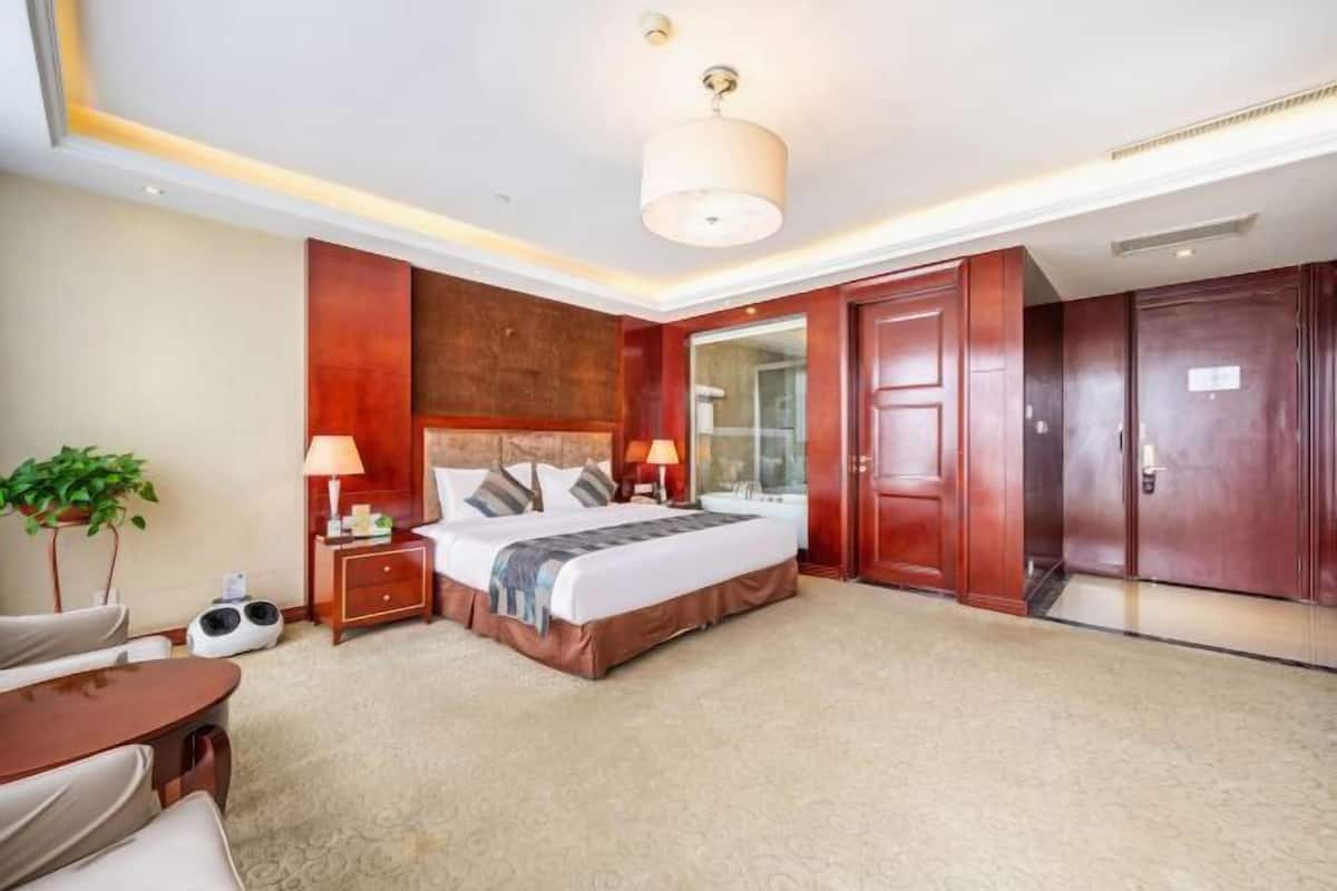 Quarto de hotel com cama grande, mesas de cabeceira, escrivaninha, cadeira, planta e guarda-roupa.