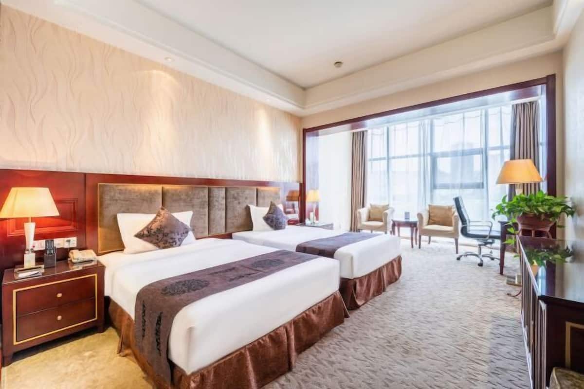 Quarto de hotel com duas camas, uma escrivaninha, uma cadeira e uma janela grande.