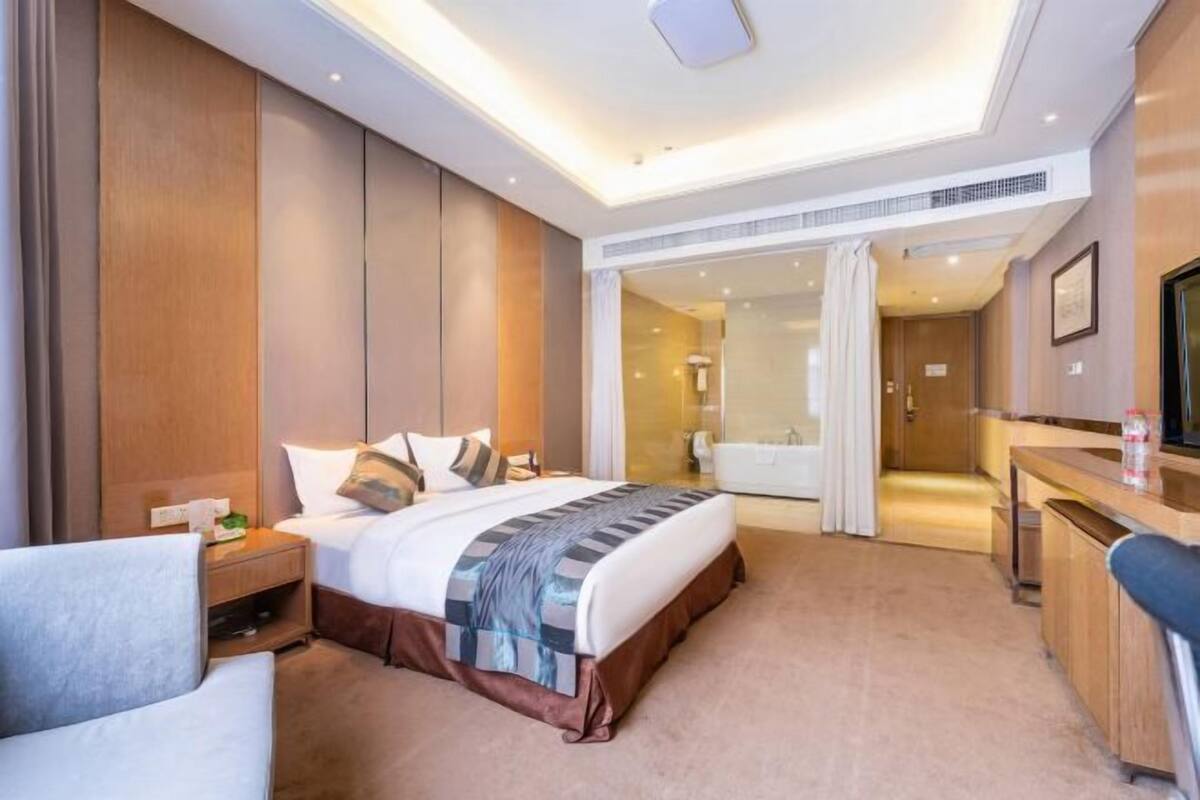 Quarto de hotel com cama, mesa de cabeceira, cadeira e banheiro visível por uma porta aberta.