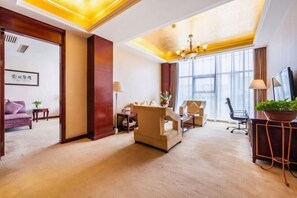 Ein Hotelzimmer mit großem Fenster, einer Kristallleuchtre, einem Sofa, einem Schreibtisch und einem Fernseher.