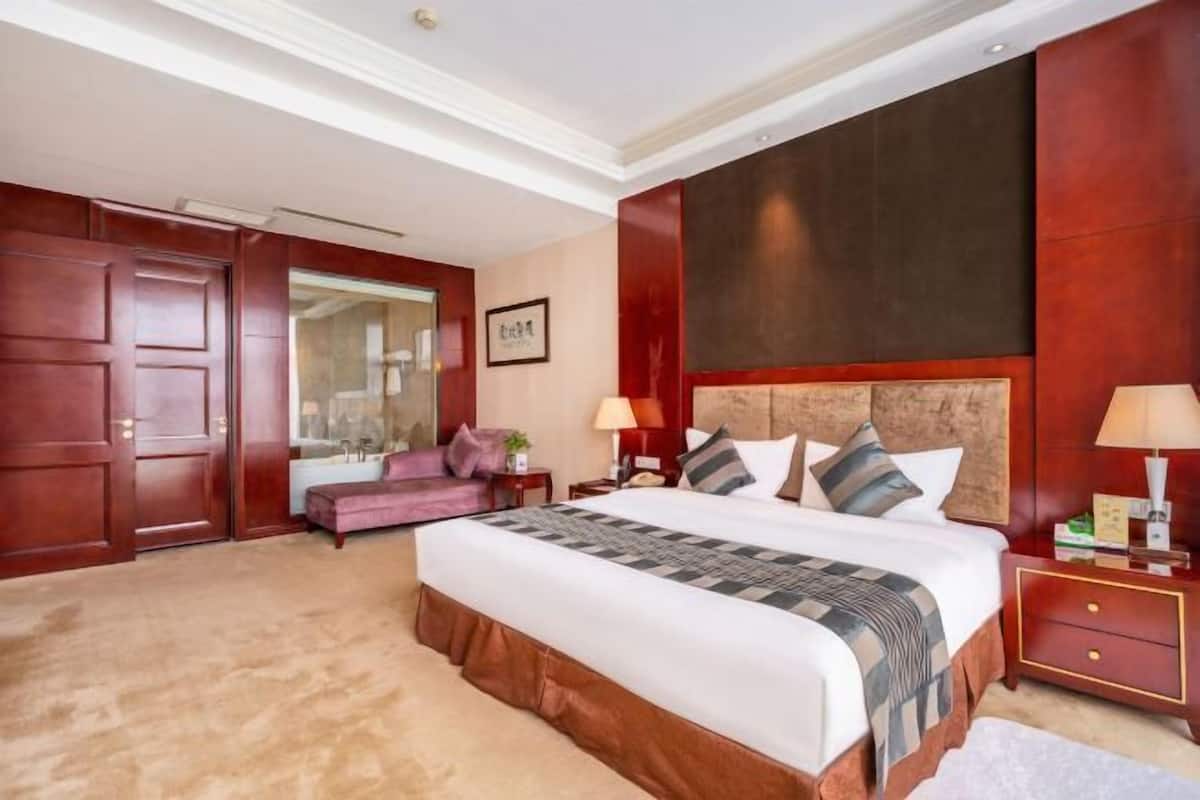 Quarto de hotel com uma cama grande, um guarda-roupa de madeira, uma toucador com espelho e um pequeno espaço de estar.